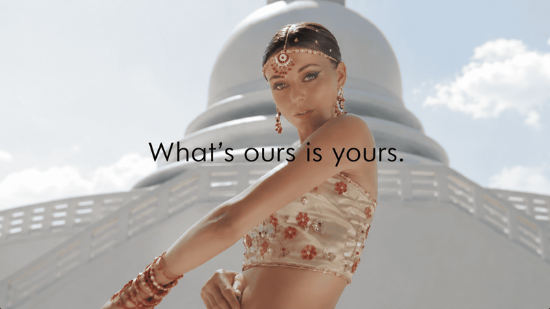 Woman wearing a designer embroidered outfit and traditional jewelry standing in front of elegant white architecture, showcasing luxury fashion rental.