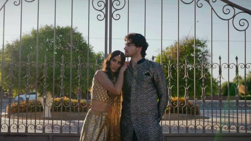 Couple wearing luxury designer formalwear available to rent from AllBorrow, standing in front of elegant wrought iron gates.